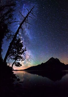 the night sky is filled with stars and clouds over a body of water that has a mountain in the distance