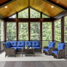 an outdoor living area with blue cushions and wicker furniture in front of large windows