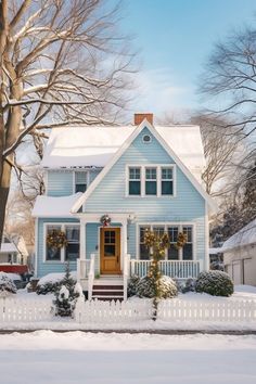 a blue house with snow on the ground and trees around it, surrounded by white picket fence