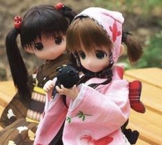 two dolls sitting on top of a wooden bench next to each other, one holding a black object