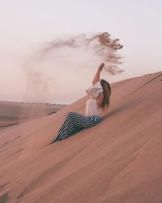 a woman sitting on top of a sand dune with her arms up in the air