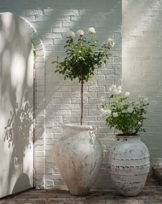 two white vases sitting next to each other on top of a brick floor near a wall