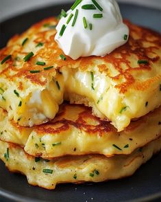 a stack of pancakes topped with whipped cream and chives on a black plate, ready to be eaten