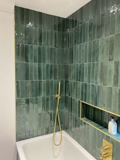 a bathtub with green tiles and gold faucet next to shelves on the wall