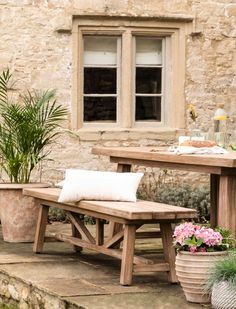 a wooden bench sitting in front of a stone building with potted plants on it