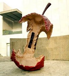 a sculpture of a baseball bat and an apple on the ground in front of a building