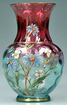 a glass vase with flowers painted on the side and gold trimming around the bottom