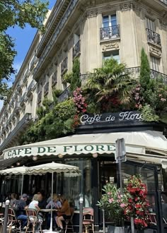 people sitting at tables in front of a building with plants growing on the side of it