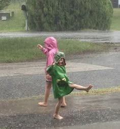 two children are playing in the rain with an umbrella and one is wearing a green raincoat