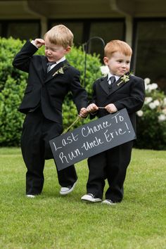 two young boys dressed in black suits holding a sign