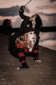 two people dressed in costumes on the beach at dusk with one person holding a stick