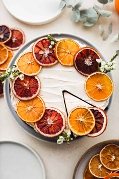 an orange cake with white frosting surrounded by sliced oranges and other citrus fruits