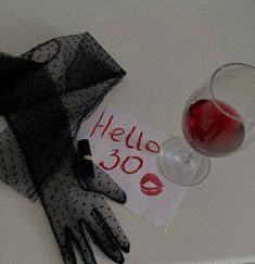 a glass of red wine next to gloves and a sign that says hello 30 on it