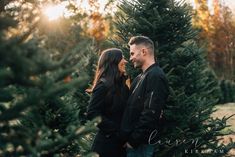 an engaged couple standing next to each other in front of a christmas tree at sunset