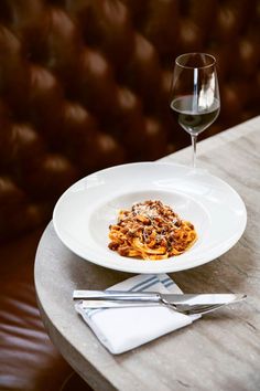 a white plate topped with pasta and sauce next to a glass of wine on a table