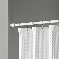 a white curtain hanging on a rod in front of a gray wall with a window