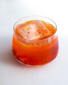 an orange drink in a glass with ice and garnish on the rim, sitting on a white surface