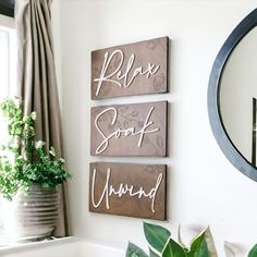 three wooden signs are hanging on the wall in front of a mirror and potted plant