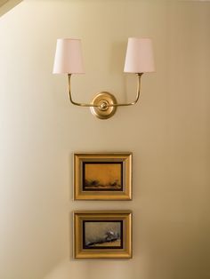 two framed pictures hang on the wall next to a light fixture and lamp in a living room