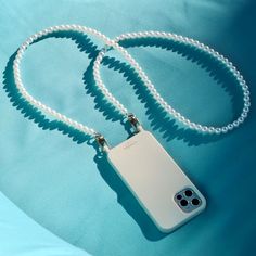 a white cell phone case is attached to a necklace on a light blue cloth background