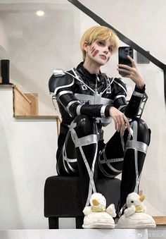 a man in black and white outfit sitting on top of a chair holding a cell phone