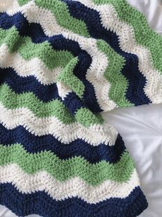 a crocheted blanket laying on top of a bed next to a white pillow