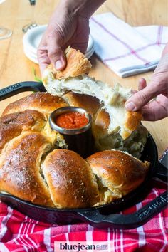 a person dipping sauce on top of bread in a cast iron skillet with red and white checkered table cloth