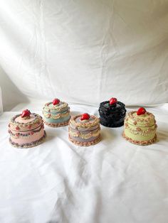 four cakes sitting on top of a white sheet covered table next to eachother