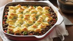 a casserole dish with meat and vegetables in it on a napkin next to plates