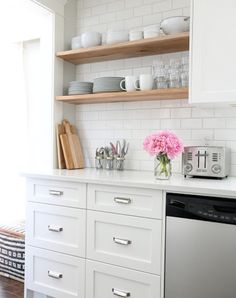 a kitchen with white cabinets and open shelving above the dishwasher is decorated with pink carnations