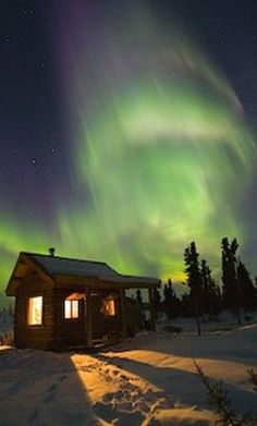 the aurora bore is shining brightly in the sky above a cabin on snow covered ground