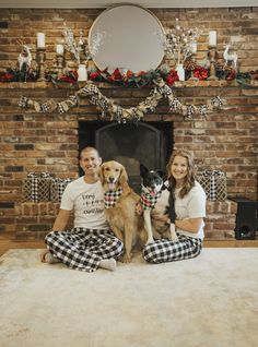 a man and woman sitting on the floor with two dogs in front of a fireplace