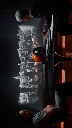 two men are working on an orange object in a room with black walls and flooring