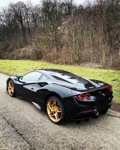 a black sports car with gold rims parked on the side of the road in front of some trees