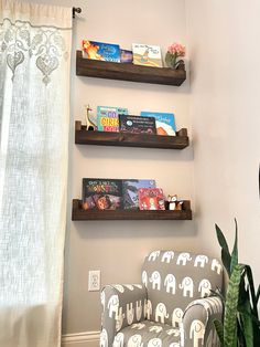 three wooden shelves with books on them above a chair in front of a curtained window