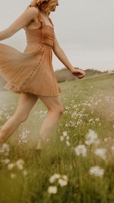 a woman in a dress walking through a field with wildflowers and grass on the ground