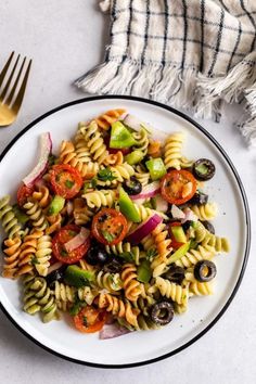 a white plate topped with pasta salad next to a fork and napkin on top of a table