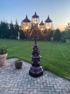 an ornate lamp post stands in the middle of a brick walkway with potted plants on either side