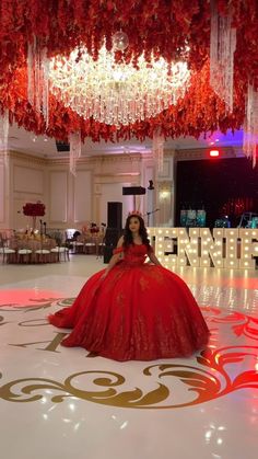 a woman in a red dress is sitting on the floor with chandelier hanging from the ceiling