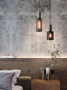 two lights hanging from the ceiling above a bed in a room with concrete walls and furniture