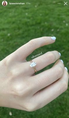 a woman's hand with a diamond ring on top of her finger and grass in the background