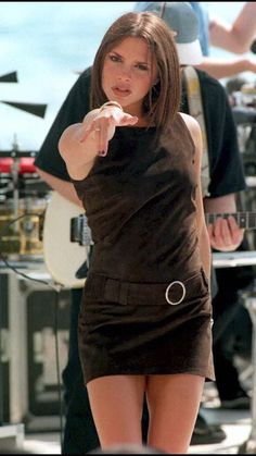 a woman in a brown dress holding a white frisbee and pointing at the camera