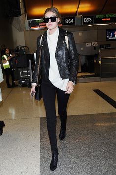 a woman is walking through an airport with her hand in her pockets and wearing black pants