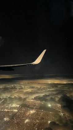 the wing of an airplane flying above the clouds at night with city lights in the distance