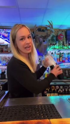 a woman is pouring something into a glass at a bar with deer head decorations on the wall behind her