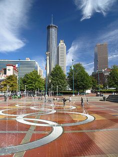 people are playing in the water fountain on a sunny day with skyscrapers in the background