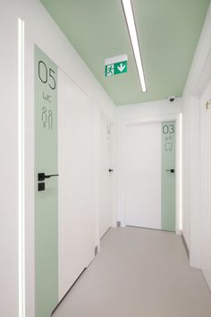 an empty hallway with white walls and green signs on the doors, leading to another room