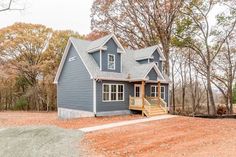 a blue house in the middle of a wooded area with lots of trees and dirt