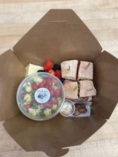 an open brown paper bag filled with food and fruit on top of a wooden table