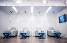 three chairs in a room with a television on the wall and two blue stools